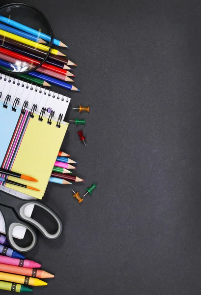 Notebook, exercise book, scissors and pencils on black board bac — Stock Photo, Image