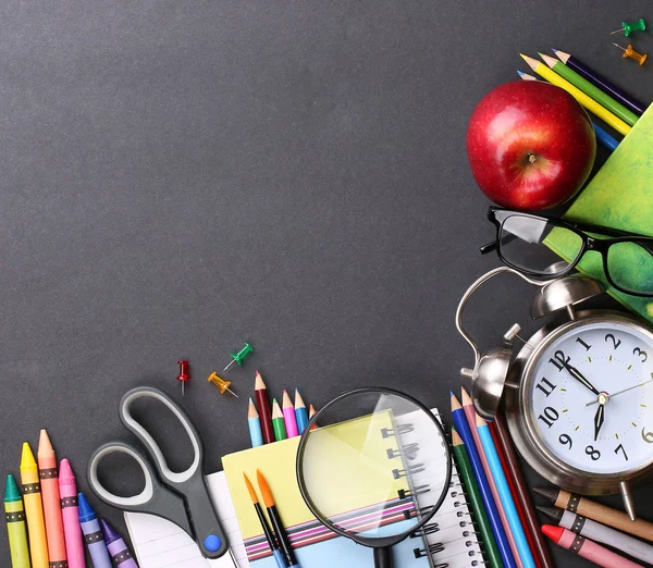 Books, apple, alarm clock and pencils on black board background. — Stock Photo, Image