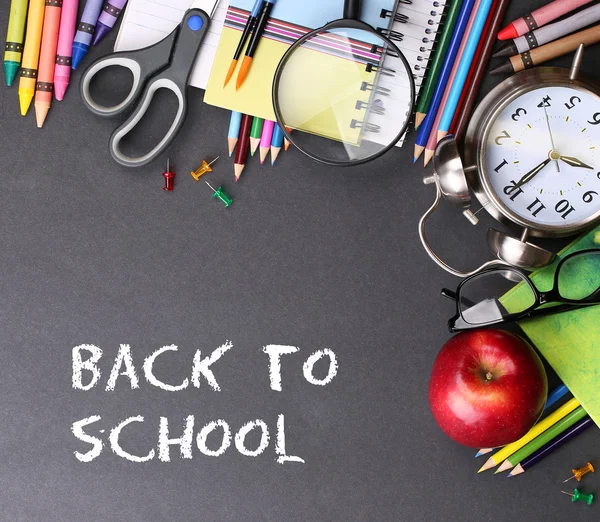 Books, apple, alarm clock and pencils on black board background — Stock Photo, Image