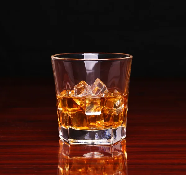 Un verre de whisky écossais alcoolisé avec glaçon sur une table en bois — Photo