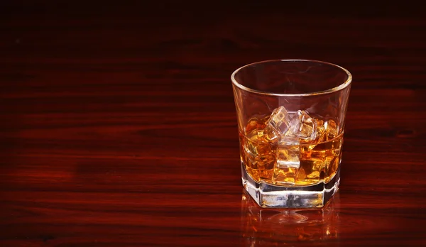 Sklenka alkoholu skotskou whisky s ice cube na dřevěný stůl — Stock fotografie