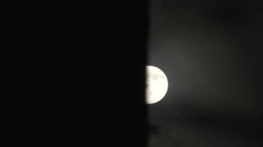 Time lapse of bright full moon appearing behind dark wall on night's sky.