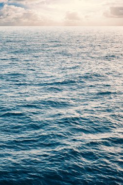 Sakin deniz ve bulutlu gökyüzü arka planda.