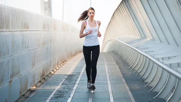 Genç bir kadın modern bir köprüde koşuyor.. — Stok fotoğraf