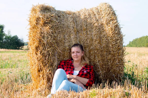 A lone woman leaned on a haystack in a field. Countryside harvesting dry grass.
