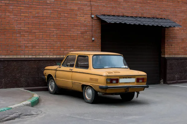 A small old Soviet car. Parked near a brick wall