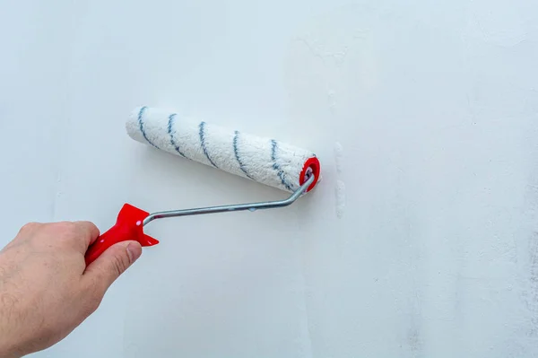 Hand with a construction roller in the process of priming the wall. The concept of renovation and decoration of the room. Antiseptic treatment. Preparing the wall for painting or wallpapering.