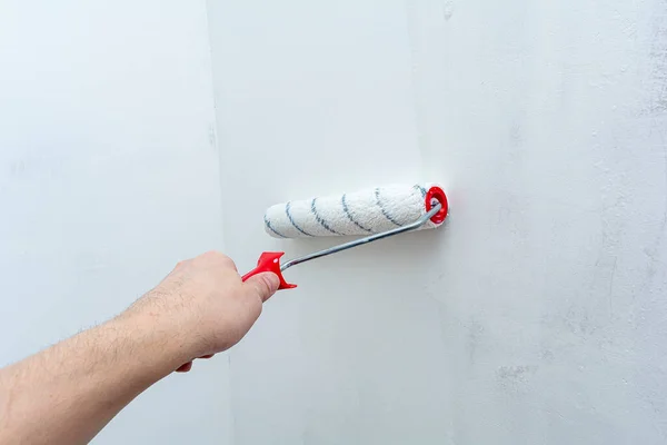 Hand with a construction roller in the process of priming the wall. The concept of renovation and decoration of the room. Antiseptic treatment. Preparing the wall for painting or wallpapering.