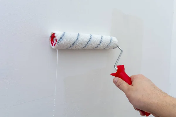 Hand with a construction roller in the process of priming the wall. The concept of renovation and decoration of the room. Antiseptic treatment. Preparing the wall for painting or wallpapering.