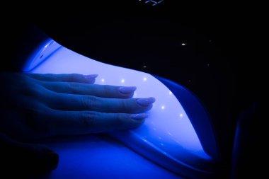 Güzel, modern manikür jölesi cilalı kadın ellerine yakından bakın. Bir kadın elini ultraviyole lambaya sokuyor. Tırnak cilasını iyileştirmek için. Yatay renk fotoğrafçılığı.