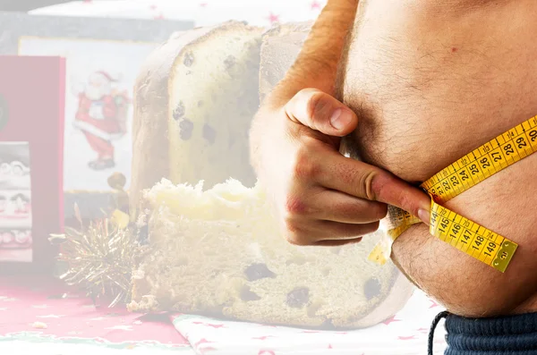 Big man measuring his belly and Christmas italian cake — Stock Photo, Image