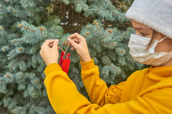 Maskeli kız Noel ağacındaki oyuncağı süslüyor.