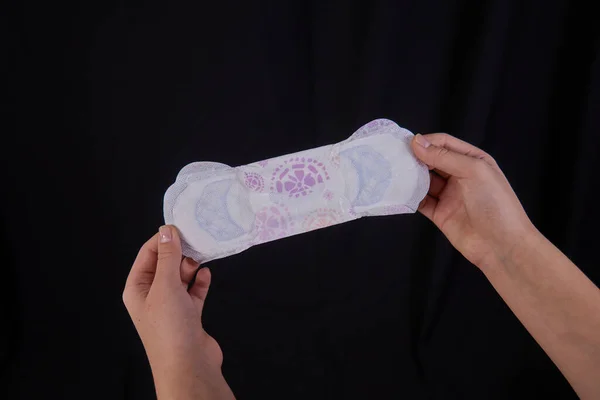 Genç bir kızın eli siyah arka planda hijyenik ped tutuyor. Yakın plan. Metin için boş boşluk.