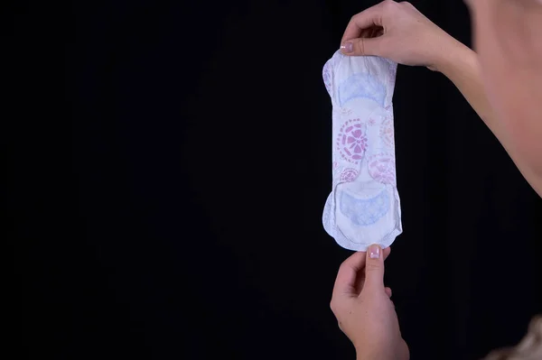 Genç bir kızın eli siyah arka planda hijyenik ped tutuyor. Yakın plan. Metin için boş boşluk.