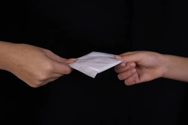 Genç bir kızın eli başka bir kıza hijyenik ped veriyor. Siyah arka plan. Yakın plan. Metin için boş boşluk.