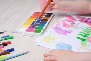 Çocuk, kağıt üzerinde bir fırçayla resim çizer, masada suluboya resimler, çocuklar için yaratıcılık, çocuklarda hayal gücünün gelişimi