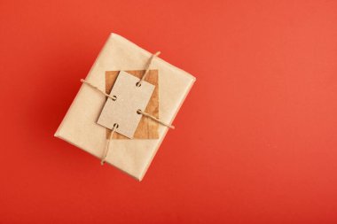 Kırmızı arka plan görünümlü Kraft kağıdına sarılı Noel hediyesi kutusu