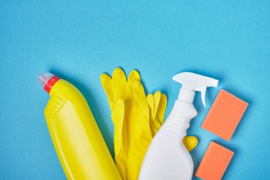 Süngerler, sarı lastik eldivenler ve mavi arka planda bir sprey şişedeki deterjan fotokopi alanı.