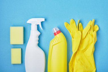 Süngerler, sarı lastik eldivenler ve mavi arka planda bir sprey şişedeki deterjan fotokopi alanı.