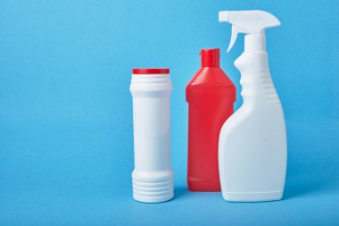 Açık mavi arka plandaki deterjanlar için etiketsiz çeşitli beyaz plastik şişeler. Fotokopi alanı, deterjan şişesi, tuvalet temizleyici ve sprey şişesi.