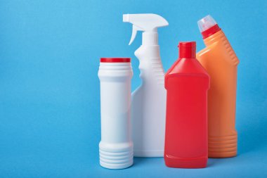 Açık mavi arka plandaki deterjanlar için etiketsiz çeşitli beyaz plastik şişeler. Fotokopi alanı, deterjan şişesi, tuvalet temizleyici ve sprey şişesi.