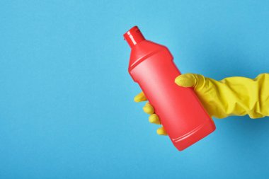 Yaşam tarzı ev bakımı konsepti. Eldivenin içindeki el, kırmızı şişeyi çamaşır jeliyle tutuyor. Etiketsiz Deterjan şişesi Kopya alanı