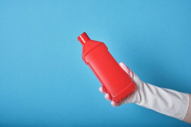 Yaşam tarzı ev bakımı konsepti. Eldivenin içindeki el, kırmızı şişeyi çamaşır jeliyle tutuyor. Etiketsiz deterjan şişesi