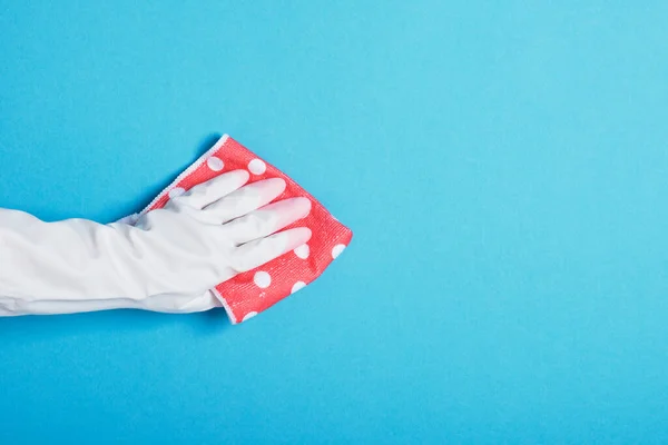 hand in white rubber glove holds pink polka dot rag, blue background