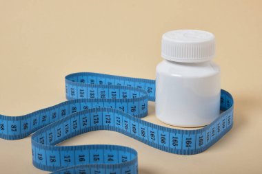 Bej arkaplan fotokopi alanı üzerinde ilaç ve mezura içeren beyaz kavanoz