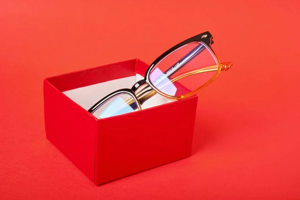 Kırmızı arka planda kırmızı hediye kutusunda gözlük. — Stok fotoğraf