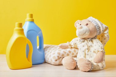 Sarı arka planda jöleli oyuncak ayı ve şişe bebek kıyafetleri yıkama konsepti.
