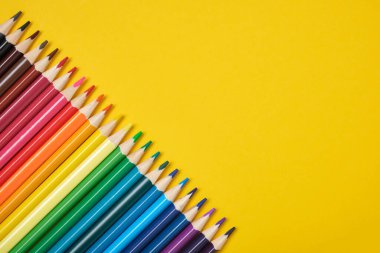 Renkli kalemler sarı bir arkaplan kopyalama boşluğunda çapraz dizilmiş.