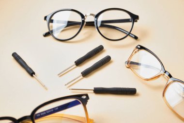 Bej arka planda birkaç çift gözlük ve küçük tornavida, kırık gözlük, gözlük onarım konsepti.