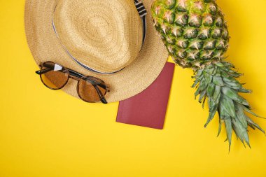 Sarı arka planda ananas, şapka, güneş gözlüğü ve uluslararası pasaport.