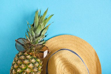 ananas güneş gözlüklü ve hasır şapkalı, mavi arka planda tropik tatil konsepti uzay üst görünümü kopyala