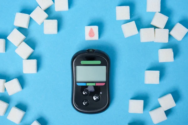 diabetes concept, sugar cube with drawn blood drop, sugar cubes and glucometer to measure blood sugar top view