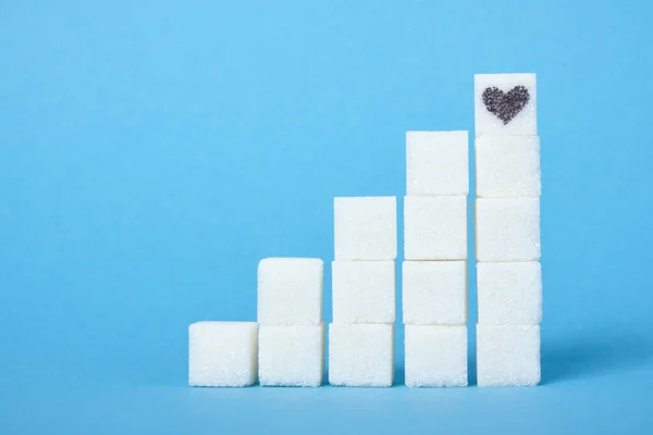 ladder of white sugar cubes on a blue background, a heart is drawn on the sugar care for health and harm of sugar concept