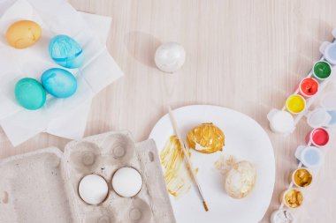 Paskalya için yumurta, yumurta kutusu, paskalya yumurtası, tabak, fırça ve boyaları ahşap masa manzarasında boyama işlemi