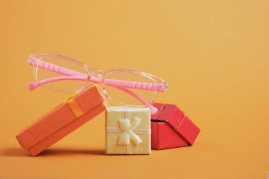 Küçük hediye kutularındaki kızlar için pembe gözlük, kahverengi arka plandaki küçük hediye kutuları fotokopi alanı, indirimler ve optik mağazasındaki promosyonlar