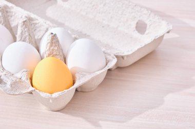 Minimum konsept Paskalya. Bir renkli yumurta ve karton bir kutuda birkaç beyaz yumurta ve masanın üzerinde ahşap bir kesme tahtası.