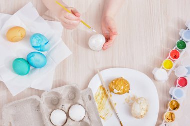 Çocuk, Paskalya için yumurtayı ahşap bir masaya boyar. Paskalya için yumurta, yumurta kutusu, paskalya yumurtası, tabak, fırça ve tablo boyama işlemi.