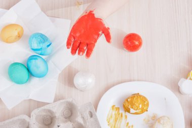 Çocuk, Paskalya için yumurtayı ahşap bir masaya boyar. Paskalya için yumurta, yumurta kutusu, paskalya yumurtası, tabak, fırça ve tablo boyama işlemi.