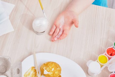 Çocuk, Paskalya için yumurtayı ahşap bir masaya boyar. Paskalya için yumurta, yumurta kutusu, paskalya yumurtası, tabak, fırça ve tablo boyama işlemi.