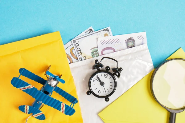 toy model of a vintage airplane made of metal, cash, several parcels, alarm clock and magnifier on blue background, air mail concept, tracking mailings concept