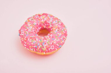 Pembe kremalı çörek ve pembe arka plan fotokopi alanına serpiştirilmiş pasta.