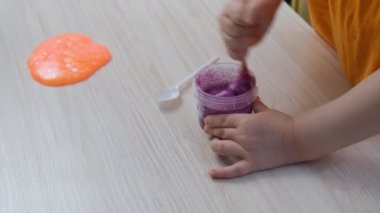 Küçük kız yanlarına pembe balçık serpiştiriyor. Çocuk elleri sümük oyuncağı oynuyor.