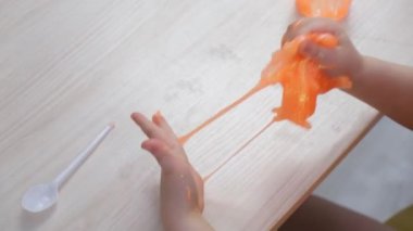 Küçük kız yanlarına pembe balçık serpiştiriyor. Çocuk elleri sümük oyuncağı oynuyor.