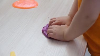 Bir çocuk ahşap bir masanın üzerindeki sümükle oynar, el ve parmakların iyi motor becerilerinin gelişmesi, çocukların ellerinde parlak bir balçık.