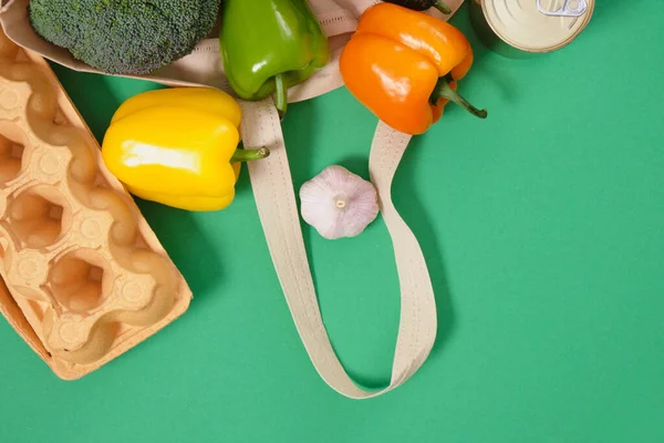 grocery food in fabric eco bag on green background top view zero waste lifestyle concept, vegetables in reusable shopping bag copy space top view