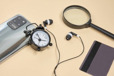 İnternetten alışveriş konsepti. Kredi kartı kulaklıklı akıllı telefon, büyüteç, bej arka planda çalar saat.